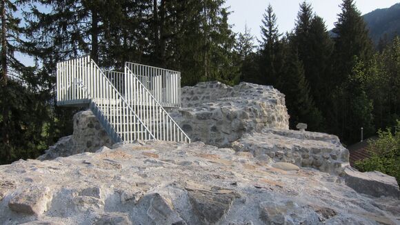 Eine Ruine mit Treppe umgeben von grünen Tannen