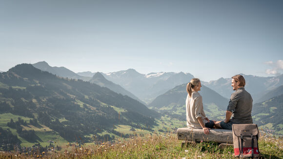 un couple est assis sur un petit banc devant le Rellerli et admire la vue sur les montagnes majestueuses au-dessus de Gstaad.