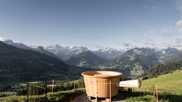 Ein hölzernes XXL Fondue Caquelon auf der Wiese mit Aussicht auf die imposante Bergwelt