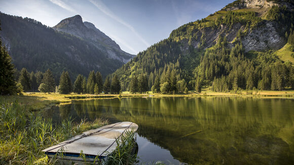 Lauenensee umgeben von Berglandschaft und Bäumen und auf dem See ist ein kleines Ruderboot zu sehen.